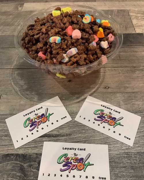 A clear bowl filled with chocolate cereal and colorful marshmallows, surrounded by loyalty cards for "The Cereal Spot."