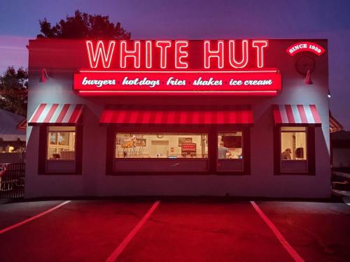 A retro diner named "White Hut" with neon signage, serving burgers, hot dogs, fries, shakes, and ice cream.