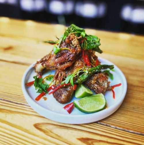 A plate of crispy fried fish garnished with herbs, chili, and lime wedges on a wooden table.