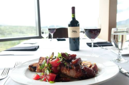 A gourmet meal with meat, garnished with herbs and fruit, accompanied by red wine and water in an elegant dining setting.