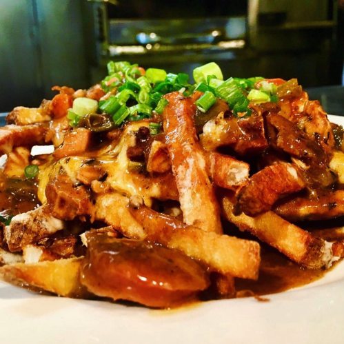 A plate of fries topped with gravy and chopped green onions, served in a warm, inviting setting.