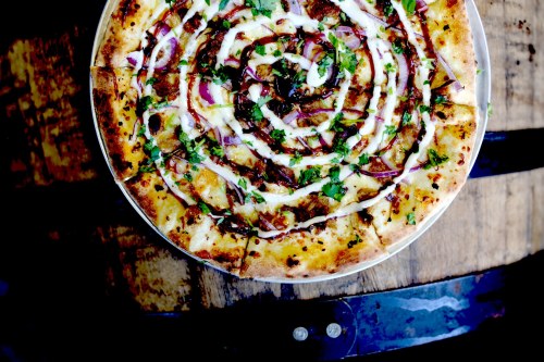 A circular pizza topped with swirls of sauce, herbs, and red onions, placed on a wooden surface.