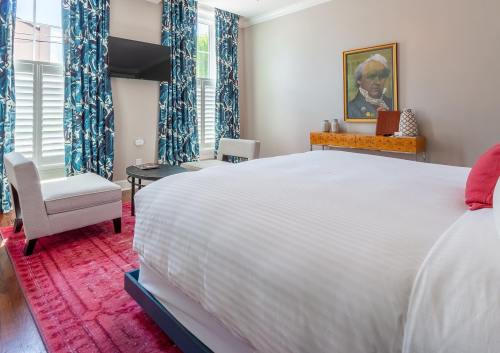 A bright hotel room featuring a large bed, colorful curtains, a seating area, and a wall-mounted TV.