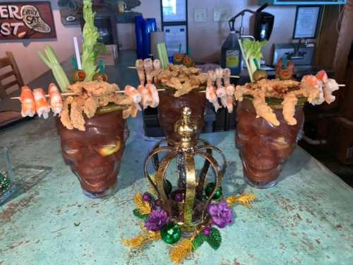 Three large, decorative cocktails with shrimp, celery, and fried food garnishes, placed on a table with a crown centerpiece.