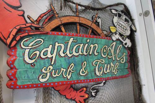 Colorful sign for "Captain Al's Surf & Turf" featuring a crab and a cartoon cow, set against a nautical background.