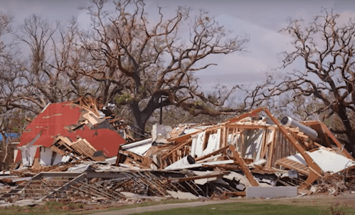 A devastated landscape showing the remains of a collapsed building surrounded by bare trees.