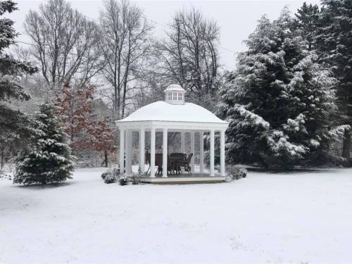 A snow-covered gazebo surrounded by trees in a winter landscape.