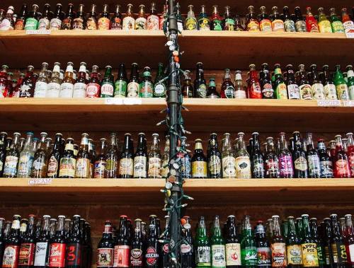 A wooden shelf filled with a variety of colorful soda bottles, neatly arranged in rows.