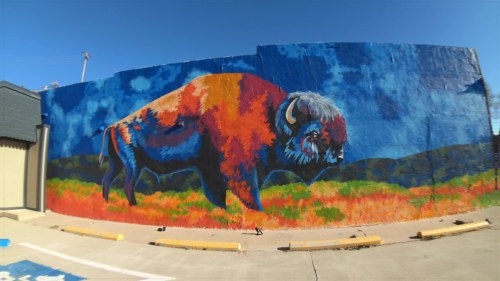 A vibrant mural of a bison against a blue sky, set in a colorful landscape with orange and green hues.