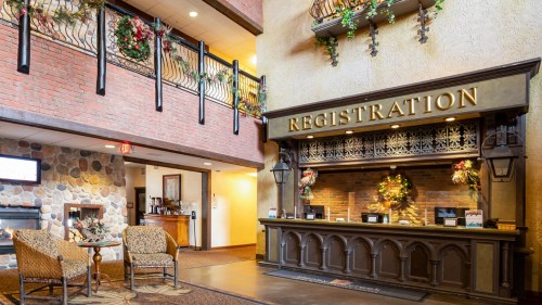 Cozy hotel lobby with a registration desk, decorative plants, and seating area, featuring warm lighting and rustic decor.