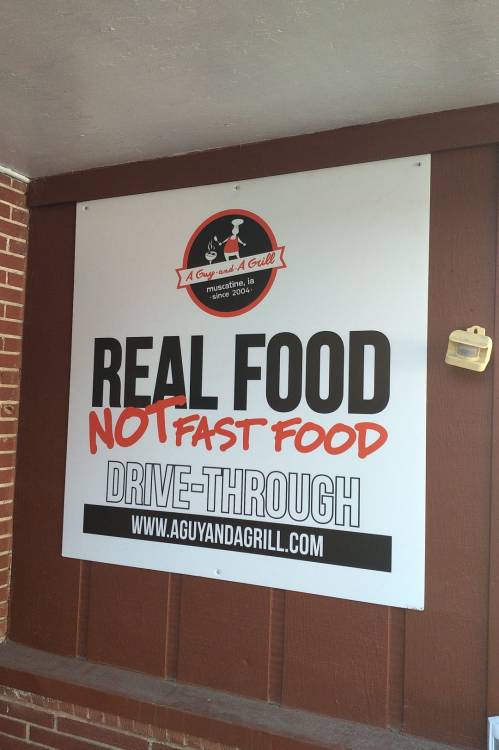 Sign promoting a drive-through restaurant, emphasizing "Real Food, Not Fast Food" with the name and website displayed.