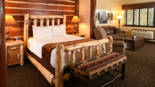 Cozy log cabin-style hotel room with a wooden bed, armchair, and warm lighting.
