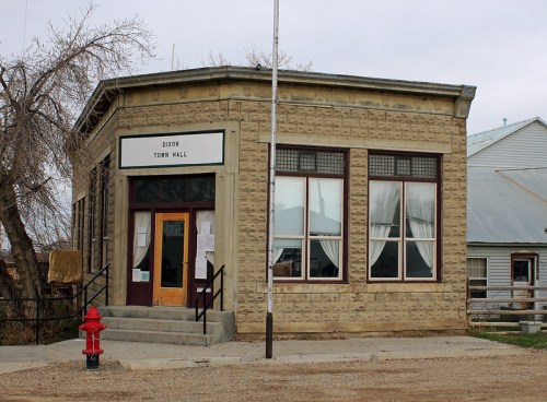 Historic building with large windows and a sign reading "Dixon Town Hall," surrounded by a rural landscape.
