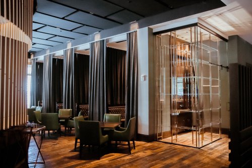 A modern restaurant interior featuring green chairs, dark curtains, and a glass display cabinet.