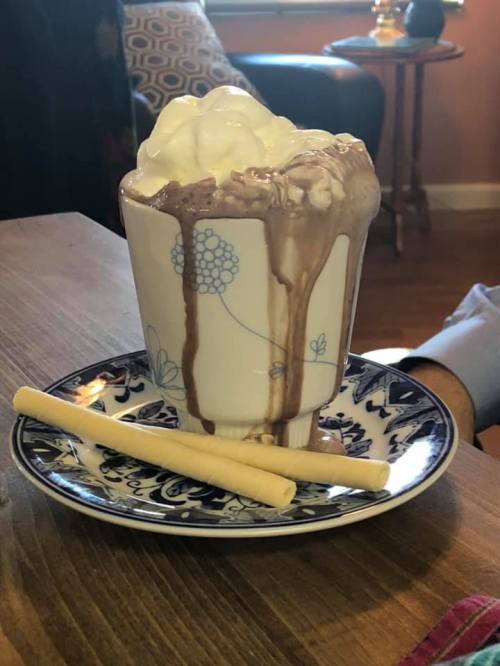 A cup of melted chocolate dessert with whipped cream, dripping down, served on a decorative plate with two sticks beside it.