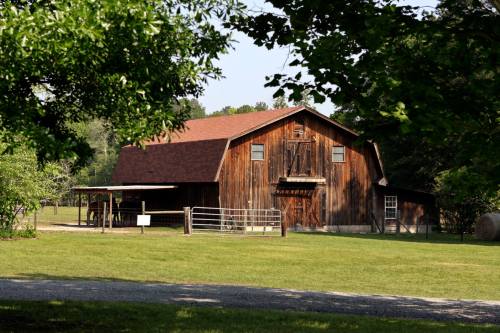 A rustic wooden barn surrounded by green grass and trees on a sunny day.