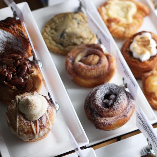 A variety of pastries displayed on a tray, including cinnamon rolls, cookies, and cream-topped treats.