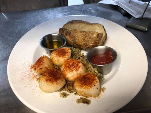 A plate with seasoned scallops on rice, a baked potato, and two dipping sauces in small cups.