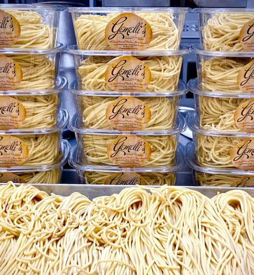 Containers of fresh pasta stacked neatly, with a focus on the smooth, golden strands of spaghetti.