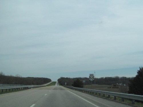 A wide, empty highway stretches into the distance, with a speed limit sign reading 50 mph on the right.
