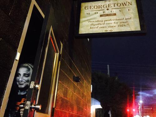 A spooky figure peeks out from the doorway of the Georgetown Morgue, illuminated by a streetlight at night.