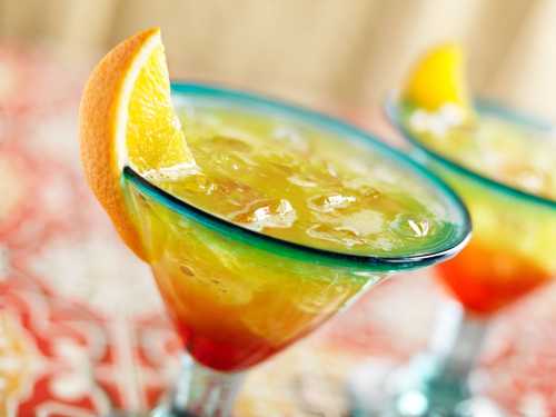 Two colorful cocktails in glasses, garnished with orange slices, on a vibrant patterned tablecloth.