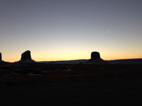 Silhouetted rock formations against a colorful sunset sky, with a hint of snow on the ground.