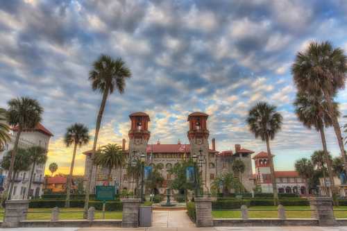 Historic building with palm trees in front, under a dramatic sky at sunset.