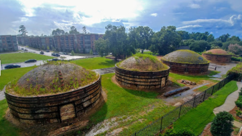 Three large, dome-shaped structures with grassy tops, surrounded by green grass and trees under a cloudy sky.