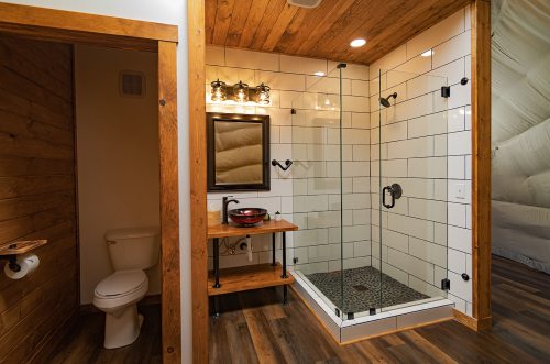 A modern bathroom featuring a glass shower, wooden accents, a sink with a mirror, and a toilet in a cozy setting.