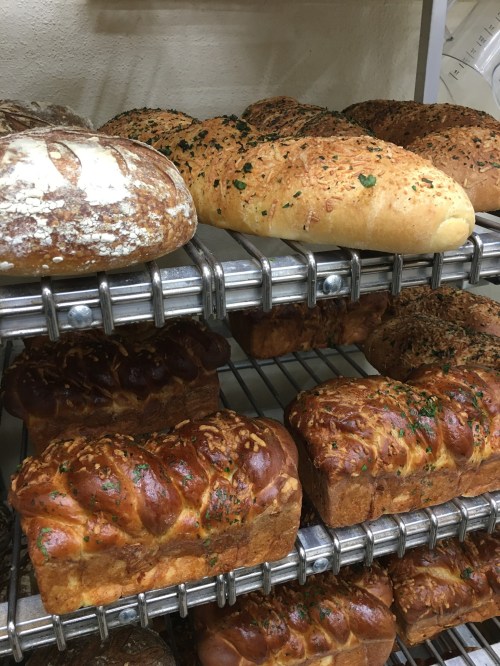 A variety of freshly baked breads on metal racks, including loaves with seeds and herbs.