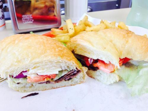A close-up of a croissant sandwich filled with vegetables and meat, served with a side of fries on a white plate.