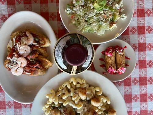 A table spread featuring shrimp pasta, a salad, macaroni, and dessert cannoli on a checkered tablecloth.