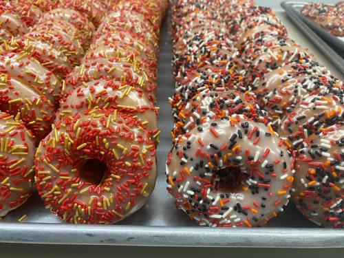 A tray of donuts topped with colorful sprinkles in red, orange, black, and white.