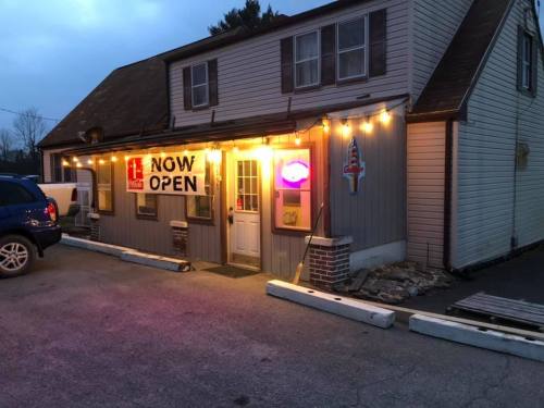 A cozy building with a "NOW OPEN" sign and string lights, welcoming customers in the evening.