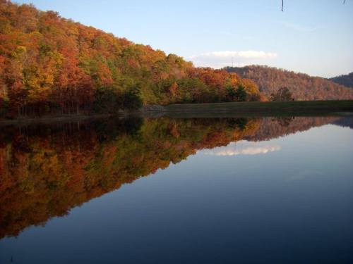 A serene lake reflecting vibrant autumn foliage and hills under a clear sky.