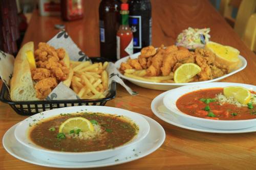 A table with fried chicken, fries, and two bowls of soup garnished with lemon and herbs. Bottles of sauce in the background.