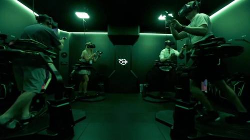 Four people in a dark room wearing VR headsets, engaged in virtual reality activities on motion platforms.