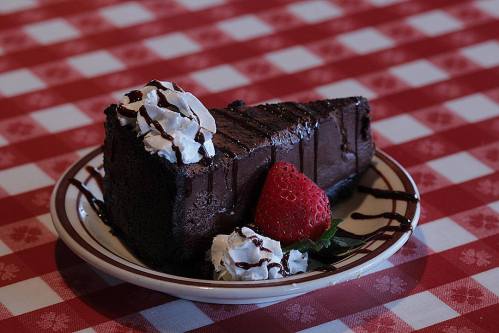 A slice of chocolate cake topped with whipped cream and a strawberry, served on a plate with a checkered tablecloth.