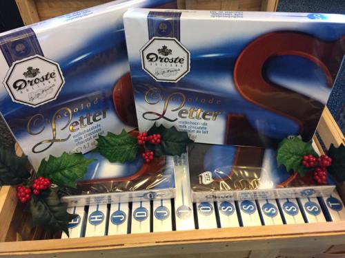 Two boxes of Droste chocolate letters in a wooden crate, decorated with holly leaves and berries.