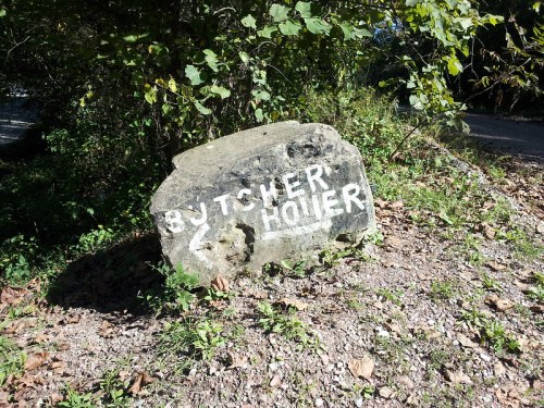 A large rock with the words "BUTCHER HOLE" painted in white, surrounded by greenery and gravel.