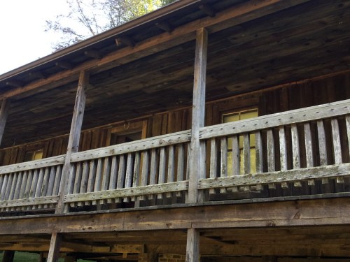 A rustic wooden cabin with a porch, featuring weathered planks and a natural setting in the background.