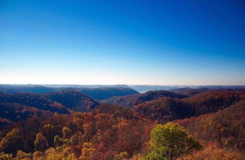 Vibrant autumn landscape with rolling hills, colorful foliage, and a clear blue sky.
