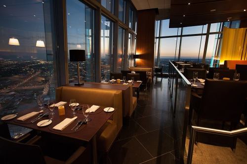 Elegant restaurant interior with dim lighting, large windows showcasing a city skyline at dusk.
