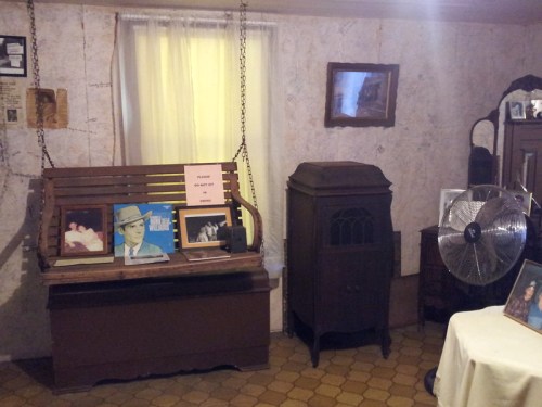 A vintage room with a wooden swing, old records, a fan, and framed photos on the walls.