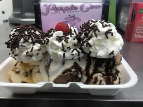 A dessert dish with three scoops of ice cream topped with whipped cream, chocolate syrup, sprinkles, and a cherry.
