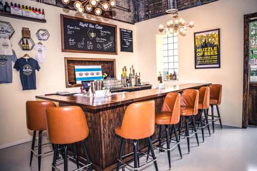 A stylish bar with brown stools, a wooden counter, and a menu board on the wall, featuring drinks and merchandise.