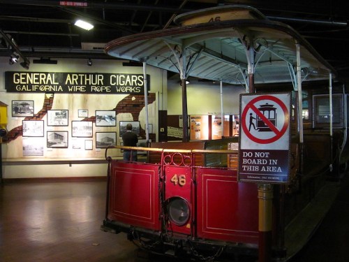 A vintage streetcar displayed in a museum, with signs about cigars and a no boarding notice.