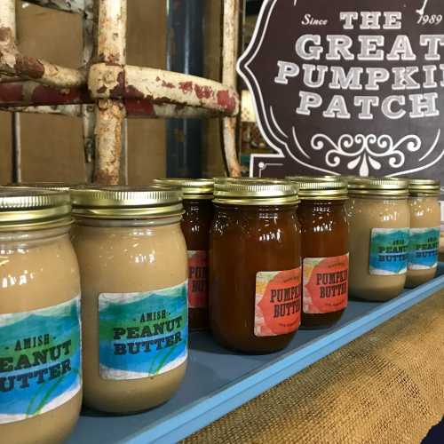 Jars of peanut butter and pumpkin butter lined up on a shelf, with a decorative sign in the background.