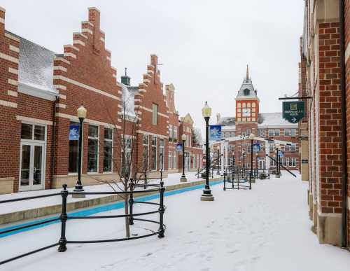 Snow-covered street lined with brick buildings and lampposts, featuring a clock tower in the background.